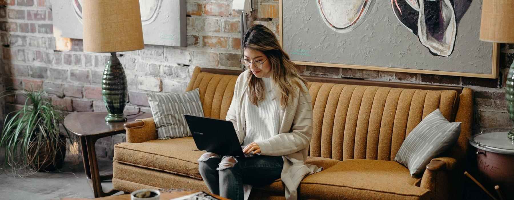 a woman sitting on a couch working on a laptop